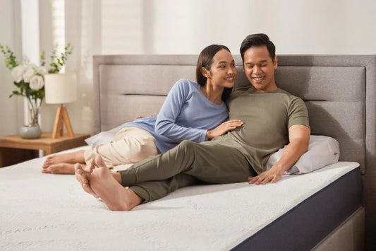 A couple sits comfortably on a Good Knight mattress. The woman gazes lovingly at the man, who smiles contentedly, both enjoying a moment of relaxation and connection.