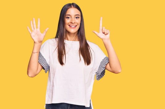 Woman showing number 7 using hand sings with bright orange yellow background
