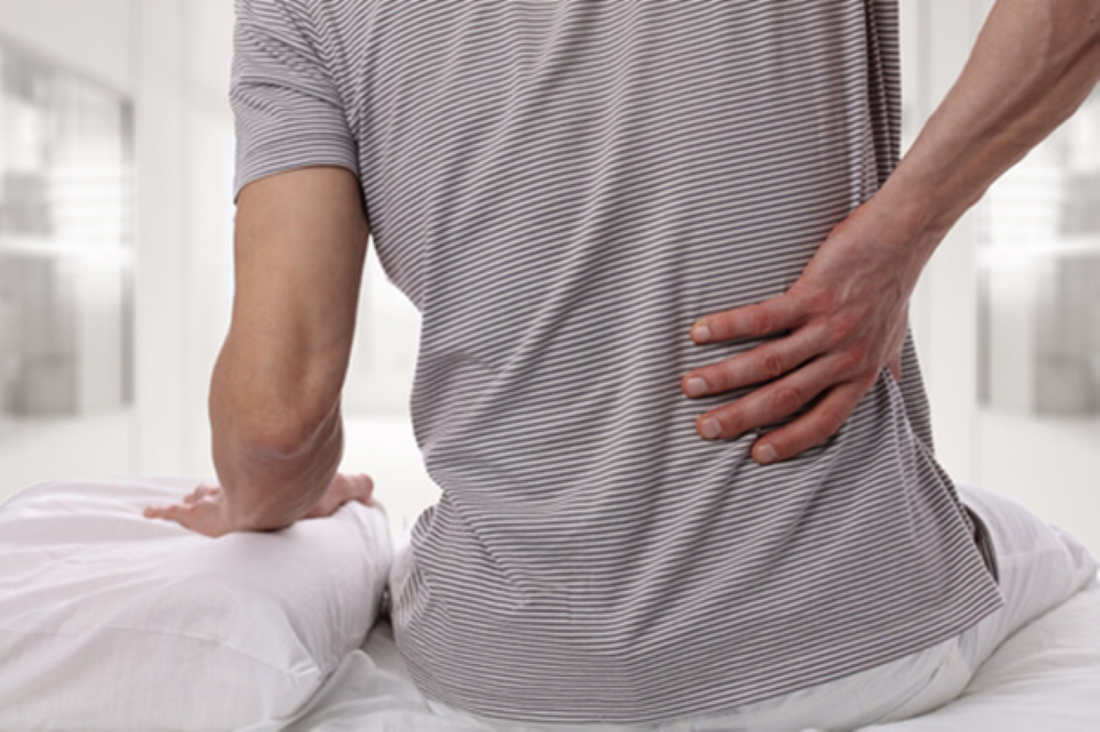Male holding his back due to back pain while sitting on his mattress