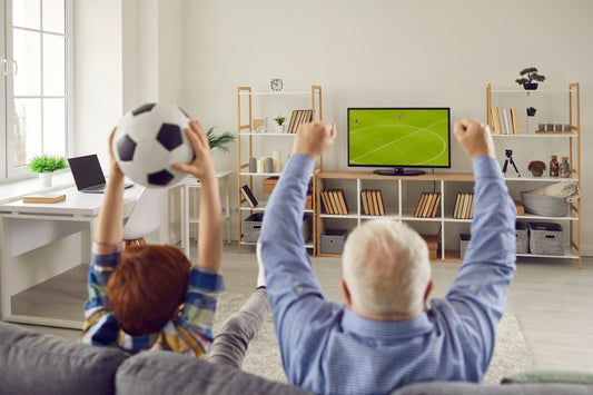 Old man and young child celebrating football match on TV while sitting on sofa in living room