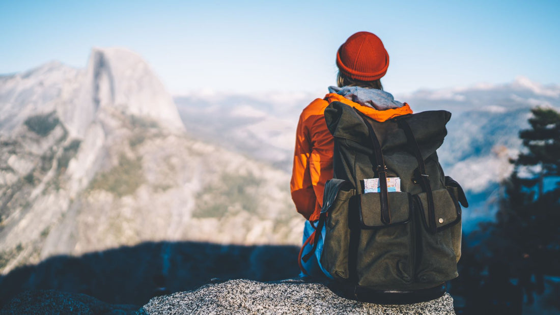 Back view of female hiker with a big black bagpack sitting on viewpoint resting during tour enjoying breathtaking landscape of high rock hills, wanderlust observe natural scenery from viewpoint.