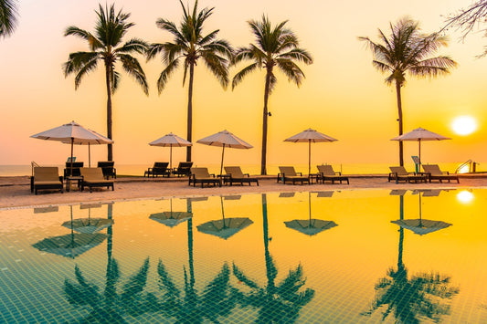 Umbrella and chair around outdoor swimming pool with sea beach ocean at sunset