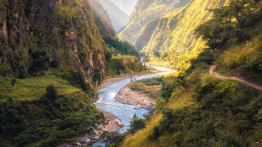 Colorful nature landscape with high Himalayan mountains, beautiful curving river, green forest, blue sky with clouds and yellow sunlight at sunset in summer in Nepal.