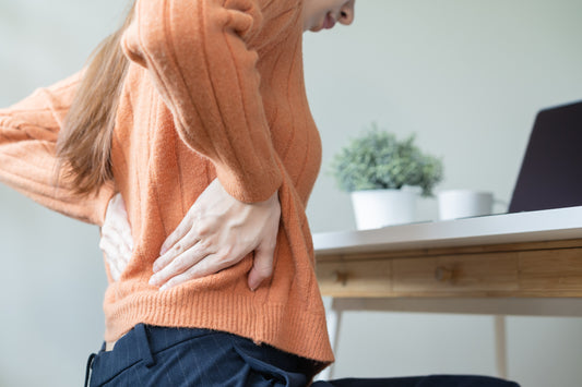 Woman wearing orange sweater and blue pants working at her desk while suffering from back pain in Singapore.