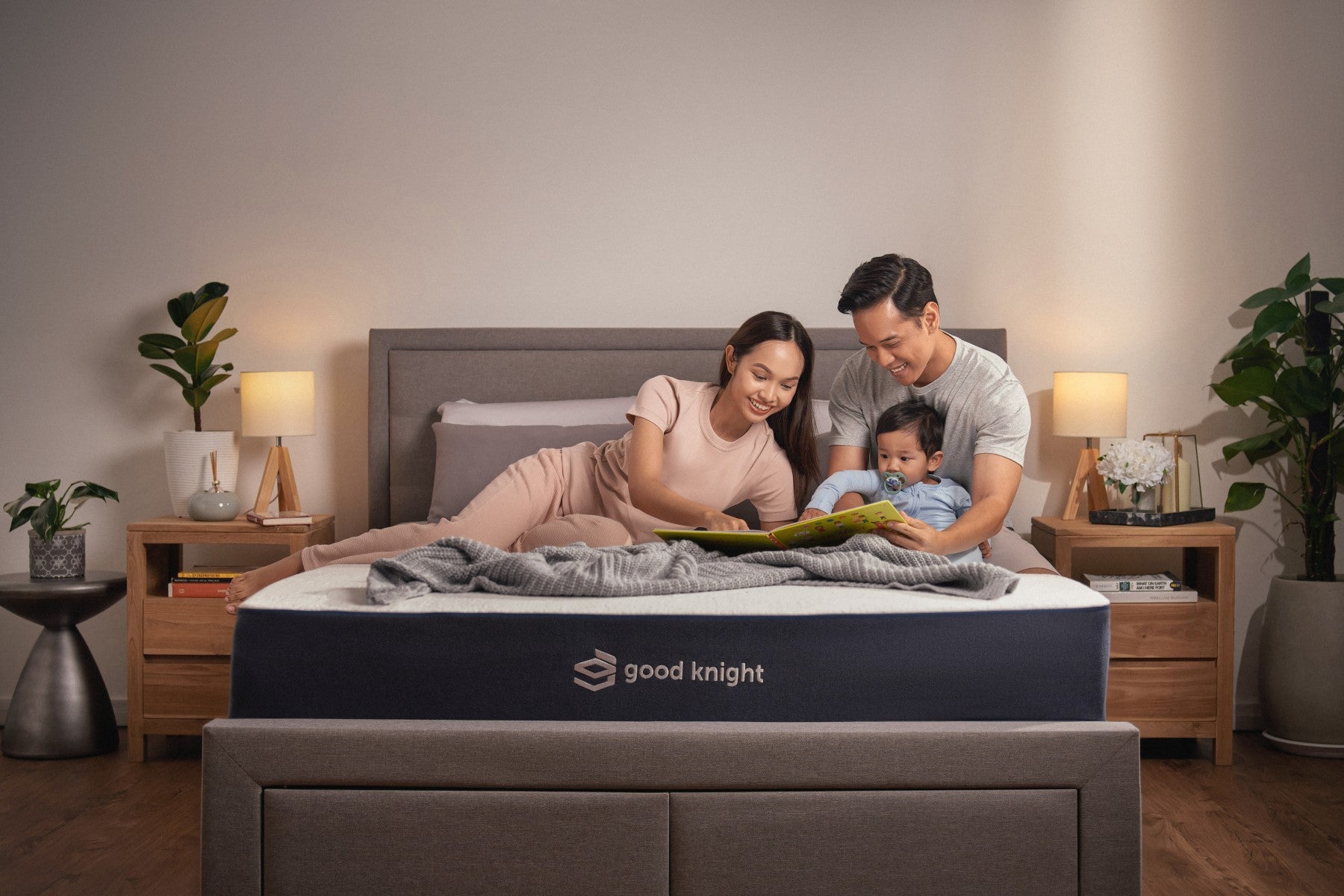 Happy family moment on a Good Knight mattress: A smiling family of three, including both parents and their little toddler, reading a bedtime story book, enjoying a moment of comfort and togetherness.